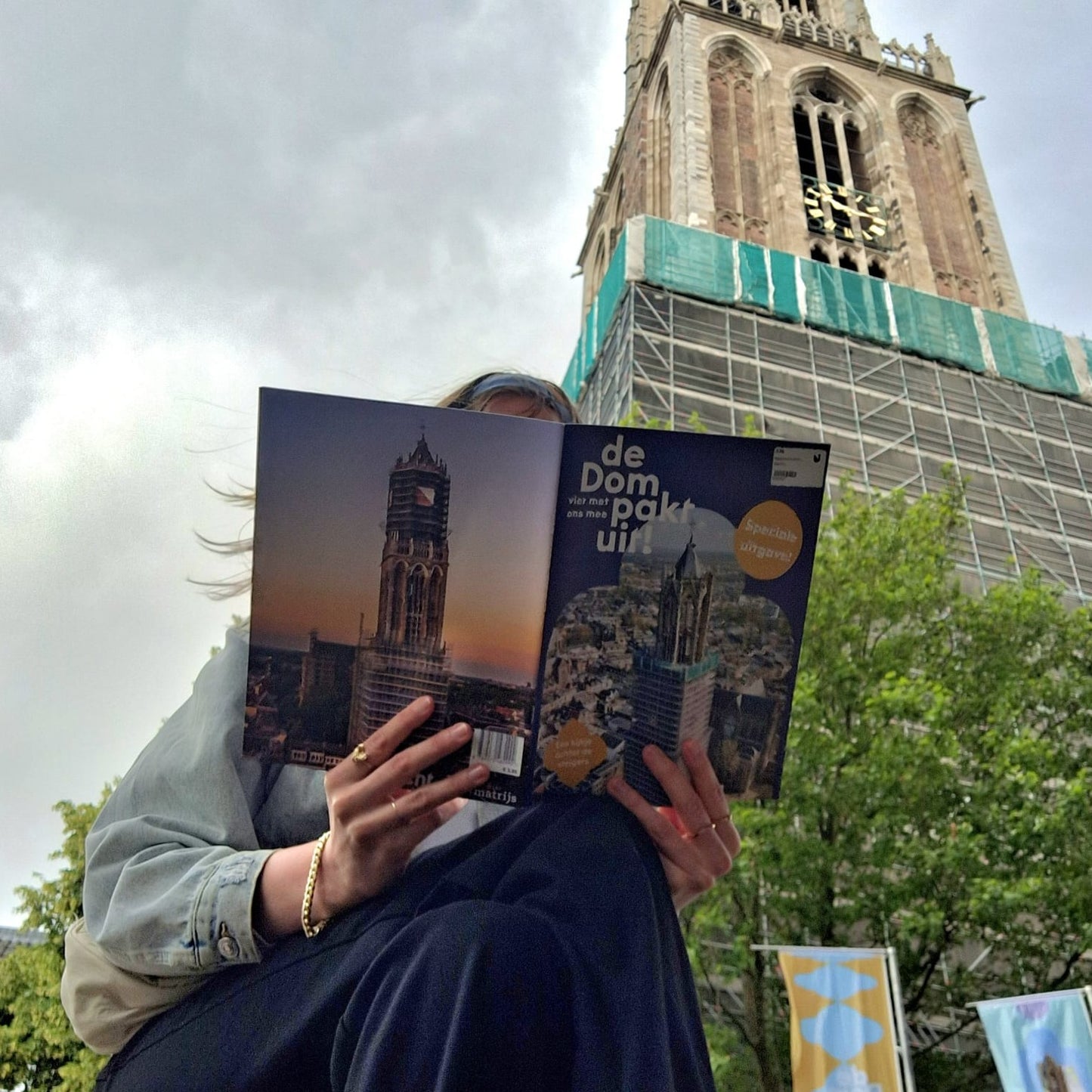 Magazine 'De Dom pakt uit!' met Domtoren op de achtergrond en iemand die het magazine leest